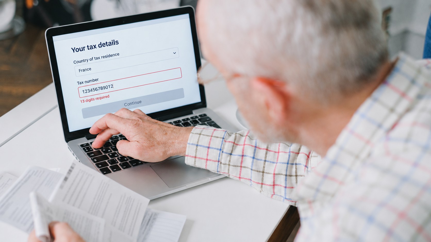 Person checking a document while an onboarding form flags an incomplete tax number.